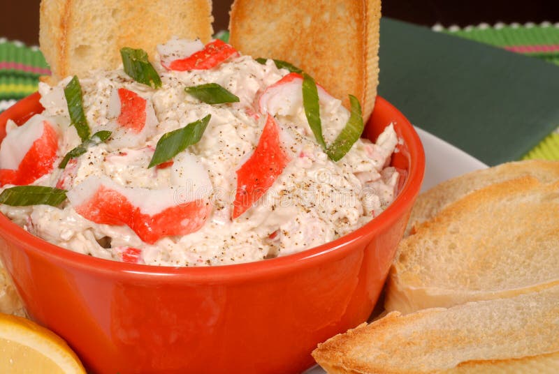 Closeup of a bowl of crab dip with toasted crostini and lemon