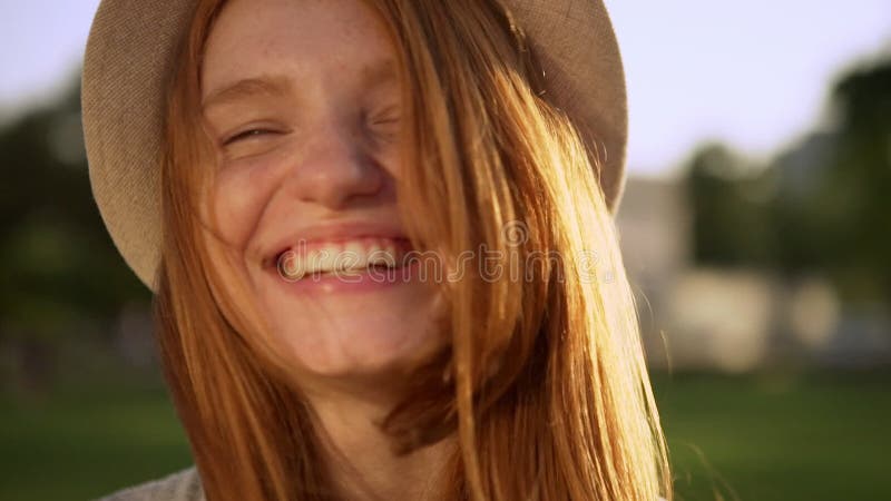 Closeup caucasian cheerful girl in hat with amazing red long hair laughing looking at camera during bright sunny day on