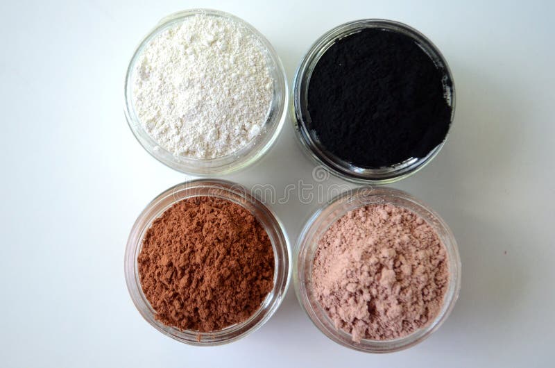 A closeup of cosmetic clays for detox face masks - French green clay, kaolin, pink clay, red clay and powdered activated charcoal