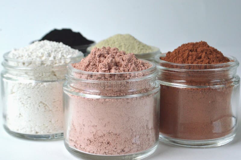 A closeup of cosmetic clays for detox face masks - French green clay, kaolin, pink clay, red clay and powdered activated charcoal