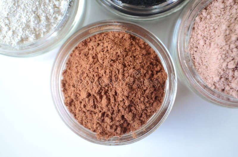 A closeup of cosmetic clays for detox face masks - French green clay, kaolin, pink clay, red clay and powdered activated charcoal