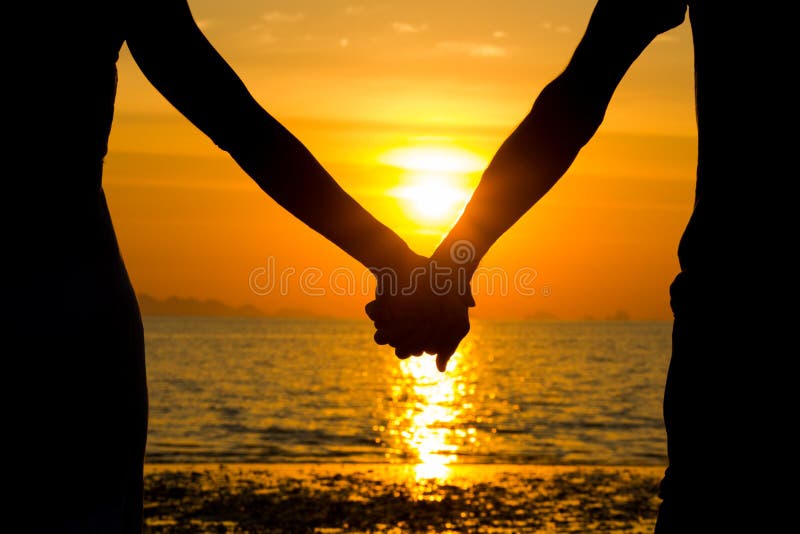 Closeup of couple silhouette holding hands at sunset by the sea