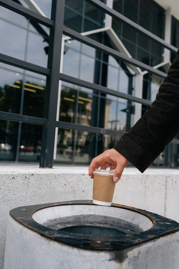 Closeup coupé d'un homme d'affaires méconnaissable jetant une tasse de café jetable dans la poubelle près du bureau photographie stock libre de droits