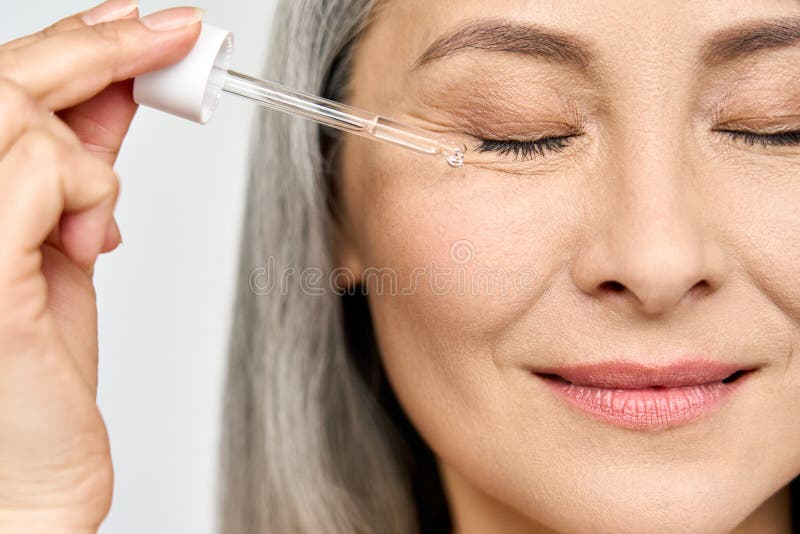 Closeup cut portrait of mature senior Asian woman with pipette serum essence.