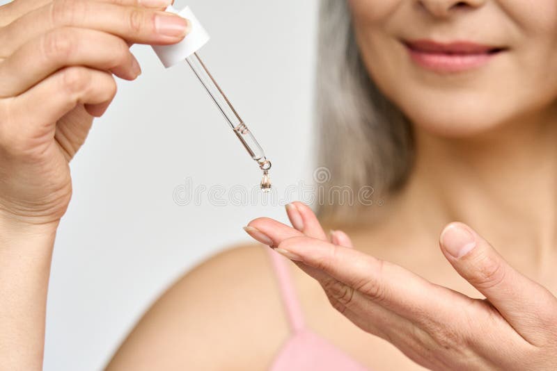 Closeup cut shot of mature Asian woman putting pipette serum essence in hand.