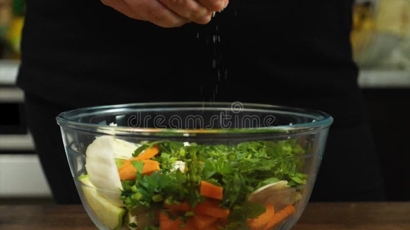 Closeup d'une femme qui arrose du sel sur une salade dans un bol de verre. mouvement lent. cuisine végétarienne. banque de vidéos