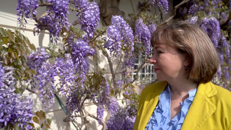 Closeup de la femme d'âge moyen entourée de fleurs de glycine florissantes. banque de vidéos