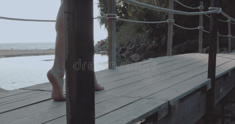 Closeup female feet walking over small wooden bridge over beach and sea background