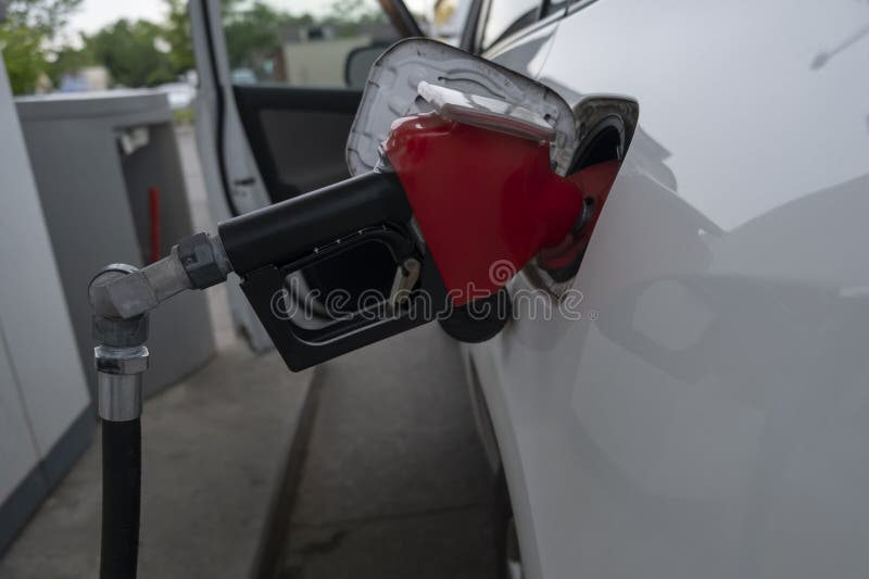 Closeup of gas station pump gun nozzle inserted into a car fuel tank filling up gasolin
