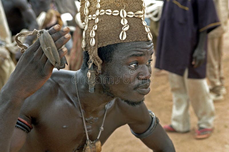 Ghana, portrait of a Ghanaian dancer, young man, in the village Savelugu. He carries out a kind of religious dance to the spirits, gods, to appease certain diseases and to cast out, superstition. Shaman. The eyes of the Ghanaian are shining and is in a kind of trans, sweating, looking out for him selves. On his cap are shells, in his hand he holds a musical instrument, a kind of castanets. In his ear, his neck and arms he wears amulets. Ghana, portrait of a Ghanaian dancer, young man, in the village Savelugu. He carries out a kind of religious dance to the spirits, gods, to appease certain diseases and to cast out, superstition. Shaman. The eyes of the Ghanaian are shining and is in a kind of trans, sweating, looking out for him selves. On his cap are shells, in his hand he holds a musical instrument, a kind of castanets. In his ear, his neck and arms he wears amulets.
