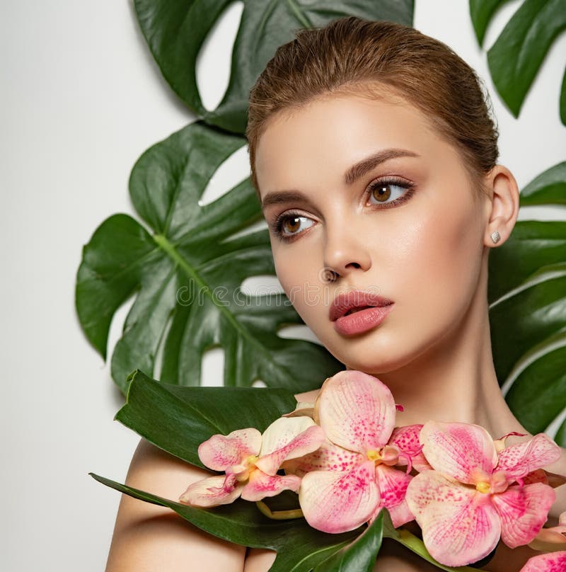 Closeup girl`s face with green leave. Model with pink tropical orchid near face. Pretty girl in Skin care beauty treatments