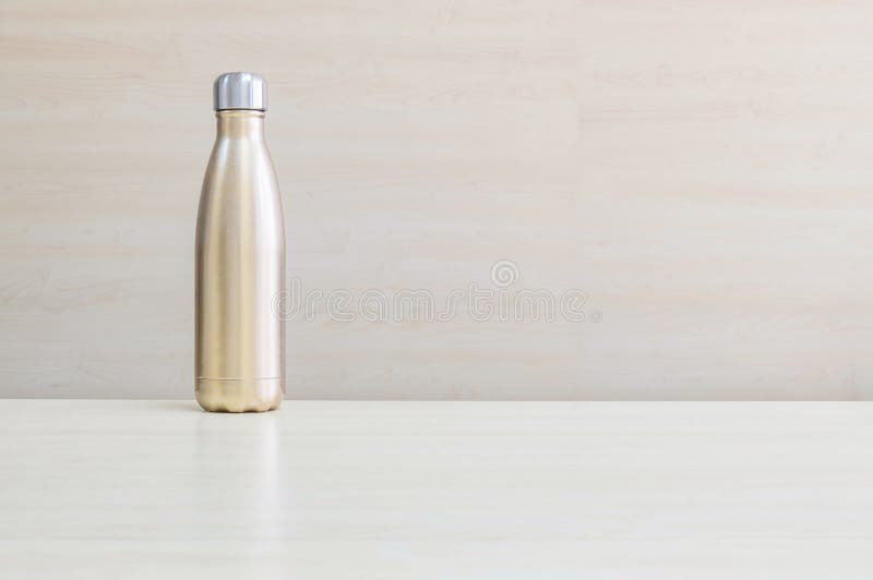 Closeup gold color of aluminium flask for keep hot water on blurred wooden desk and wall textured background under window light royalty free stock image