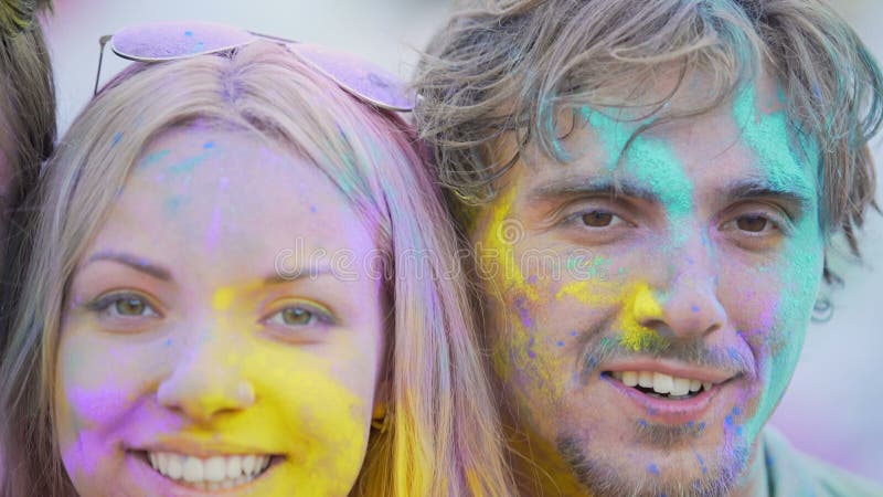 Closeup of happy male and female faces covered in colors smiling for camera