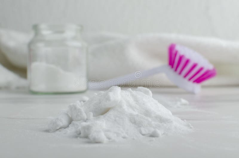 Closeup of pile of baking soda, kitchen brush, glass full of cleaning detergent and towel on the white table