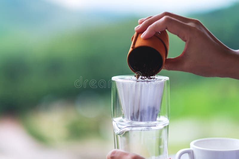 A Hand Pouring Coffee Grounds from Grinder into a Drip Coffee Filter