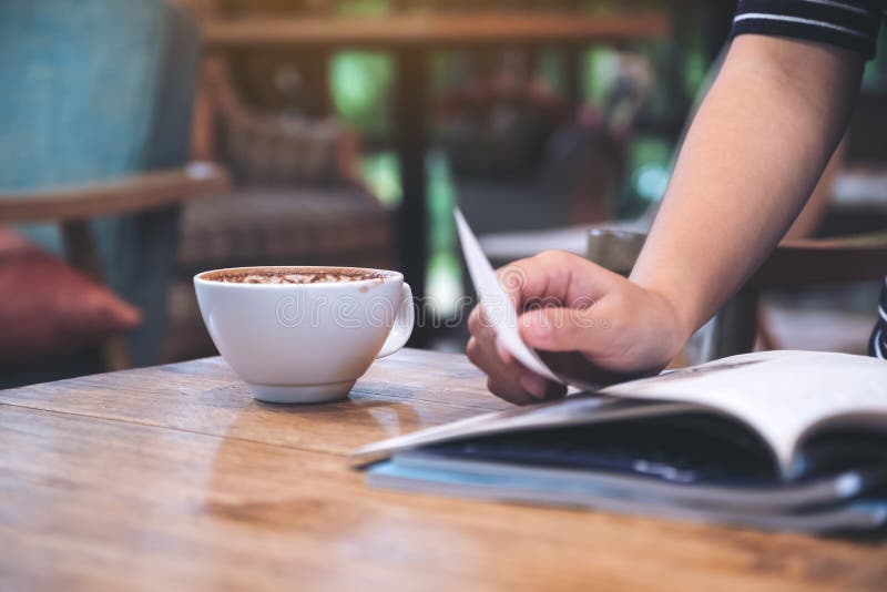 A woman reading a magazine with coffee cup on table in cafe