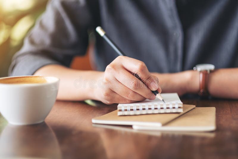 A woman`s hand writing on blank notebook with coffee cup on table in cafe stock photos A woman`s hand writing on blank notebook with coffee cup on table in cafe stock photos