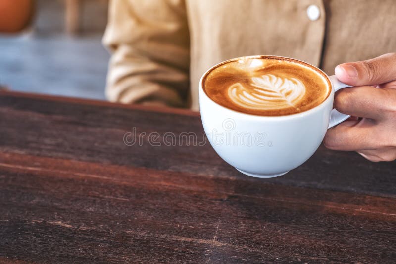 Woman`s hands holding a cup of hot coffee on wooden table in cafe