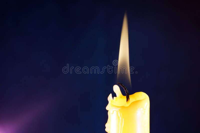 Closeup of a Lit Candle that is Slowly Melting on a Dark Blue