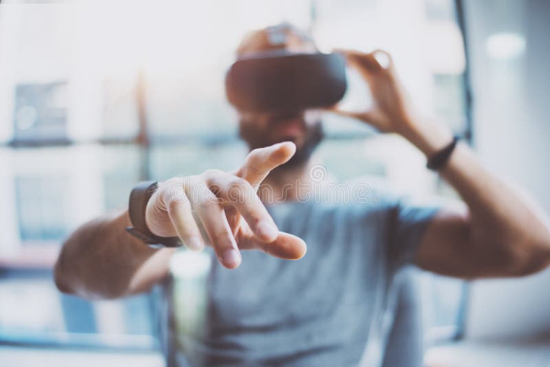 Closeup of male hand.Bearded young man wearing virtual reality goggles in modern coworking studio. Smartphone using with