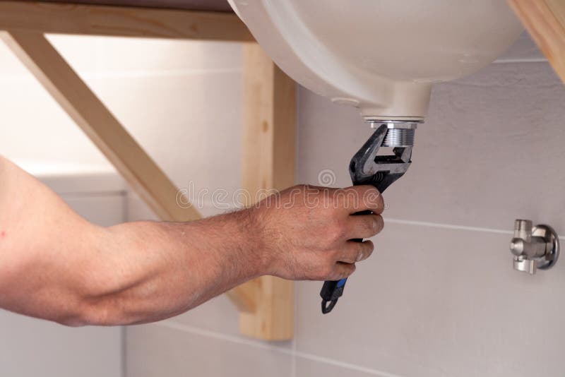 Closeup male plumber`s hand fixing sink in bathroom with tile wall. Professional plumbing repair service, installation