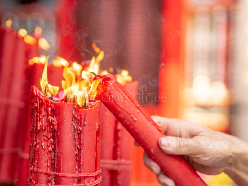 Closeup a man hand lighting a candle from bundle of big red candles burning at Longshan temple.