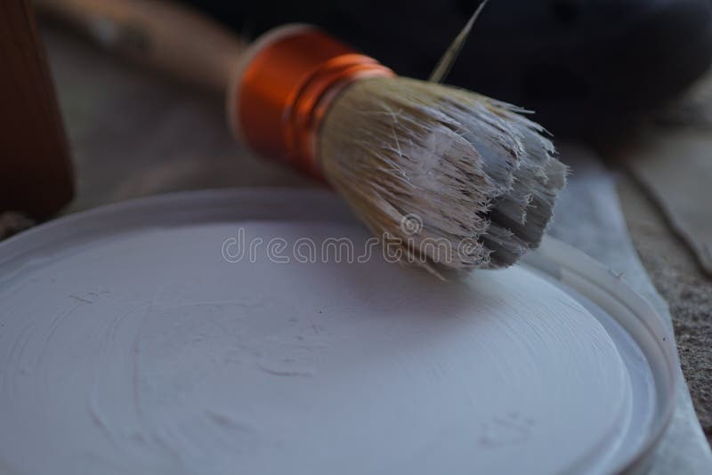 Closeup of a Paintbrush with White Dried Paint on it Next To a Lid