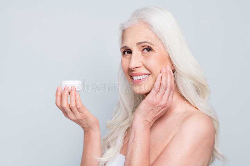 Closeup photo of beautiful old woman toothy smile applying daily nourishing anti age cream isolated grey color