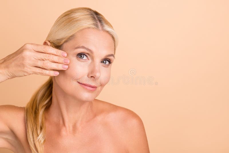 Closeup photo of natural beauty aged lady nude shoulders touch fingers cheek apply anti age uplift cream isolated beige. Color background