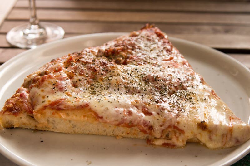 A Closeup of a Pizza Slice on a Plate with a Glass in the Background ...