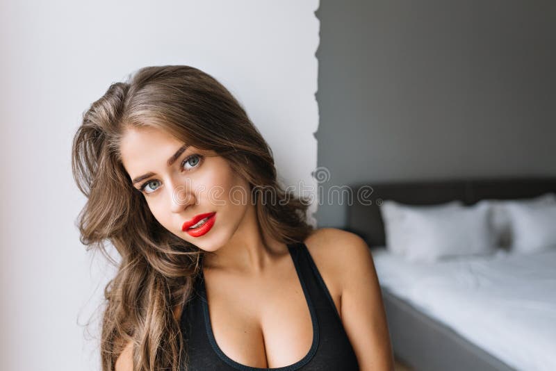 Closeup portrait attractive charming girl with long brunette hair in modern apartment. Sexy T-shirt, true emotion, red