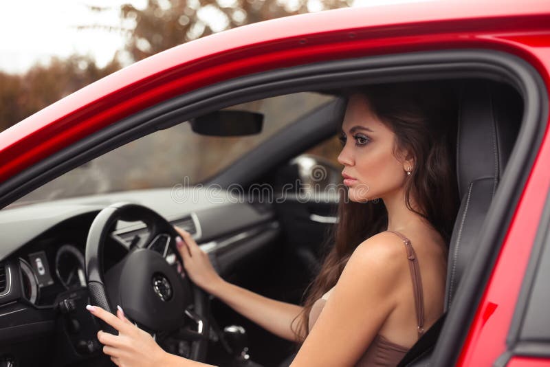 Closeup portrait of attractive young woman profile in dress looking on road while driving a red car. Confident and beautiful. Auto