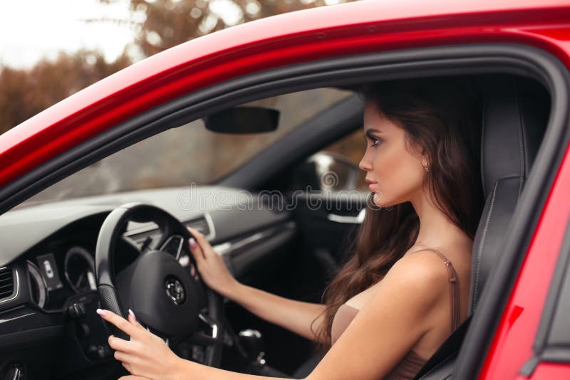 Closeup portrait of attractive young woman profile in dress looking on road while driving a red car. Confident and beautiful. Auto