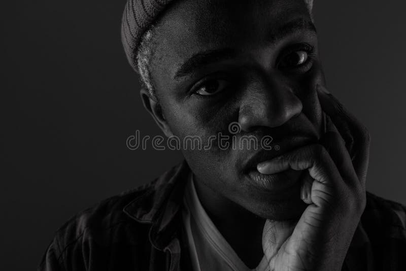 Closeup portrait of a black African man with big lips biting his finger in black and white light.