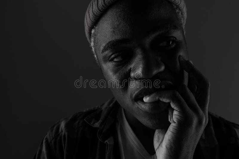 Closeup portrait of a black man with big lips biting his finger in black and white light.