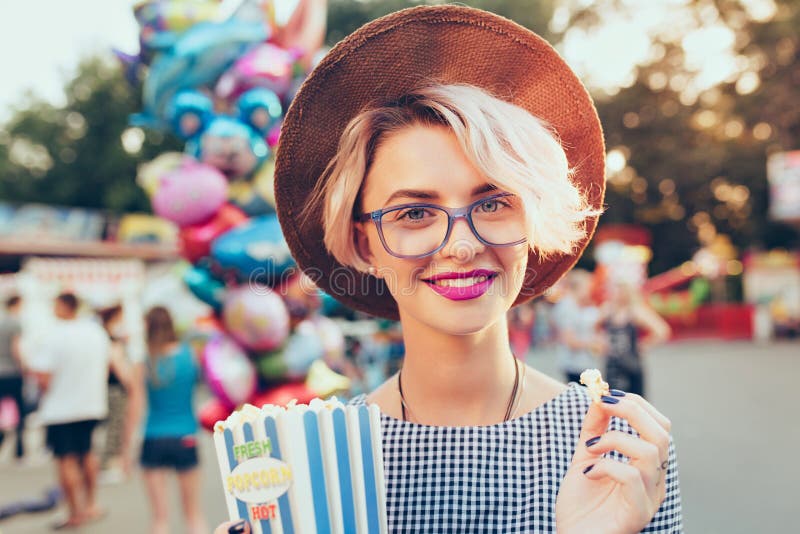 Closeup portrait of blonde girl with short haircutotdoor on baloons background. She wears checkered dress, hat, glasses