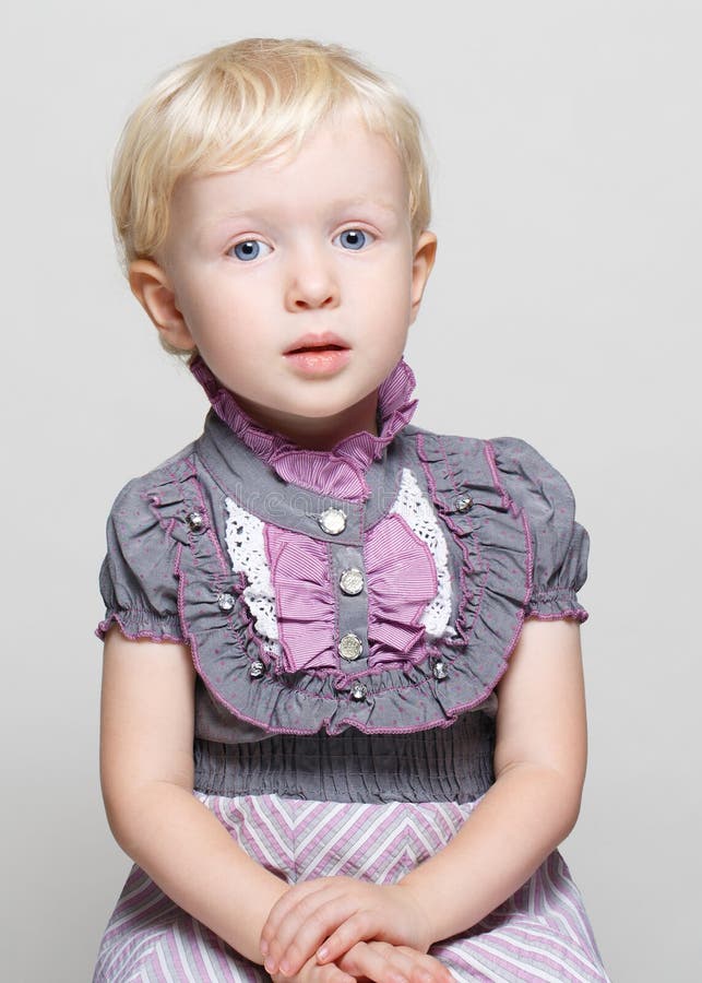 Closeup portrait of cute child toddler girl with blonde hair and blue eyes in vintage retro victorian gothic dress posing sitting