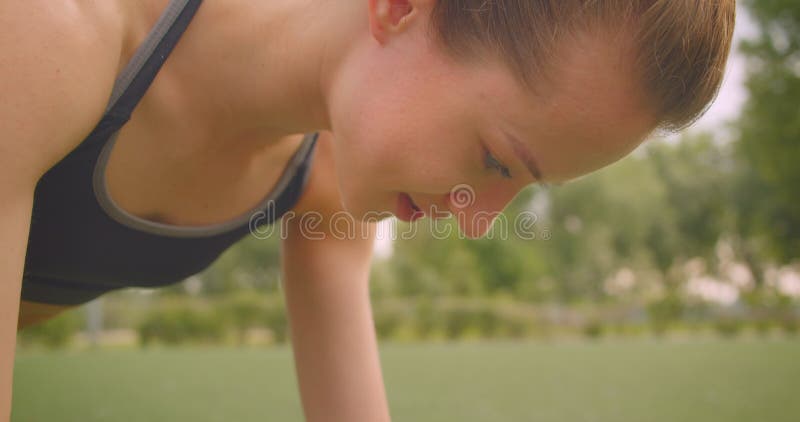 Closeup portrait of cute pretty sporty fitness girl doing plank exercise in the park in urban city outdoors