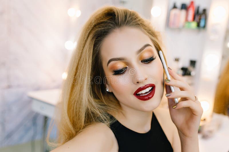 Closeup portrait fashionable model with stylish makeup speaking on phone in hairdresser salon. Preparing to party, red