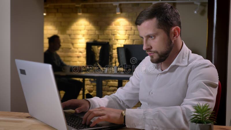 Closeup portrait of focused adult caucasian man typing on the laptop in the office indoors