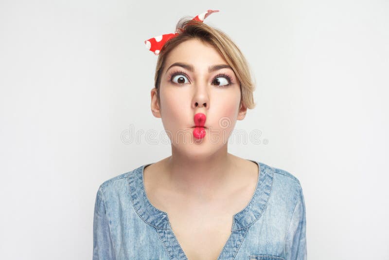 Closeup portrait of funny crazy young woman in casual blue denim shirt with makeup and red headband standing, crossed eyes with