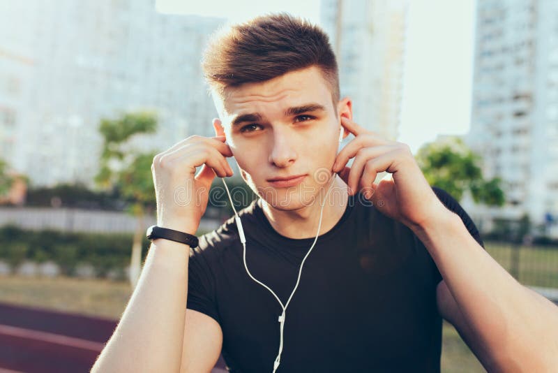 Closeup portrait of handsome guy with a good body in the morning on stadium. He wears black T-shirt, put headphones to royalty free stock images Closeup portrait of handsome guy with a good body in the morning on stadium. He wears black T-shirt, put headphones to royalty free stock images