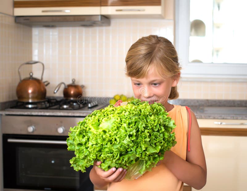 Closeup portrait of little girl holding fresh green lettuce in the kitchen. Healthy food and lifestyle concept. stock image Closeup portrait of little girl holding fresh green lettuce in the kitchen. Healthy food and lifestyle concept. stock image