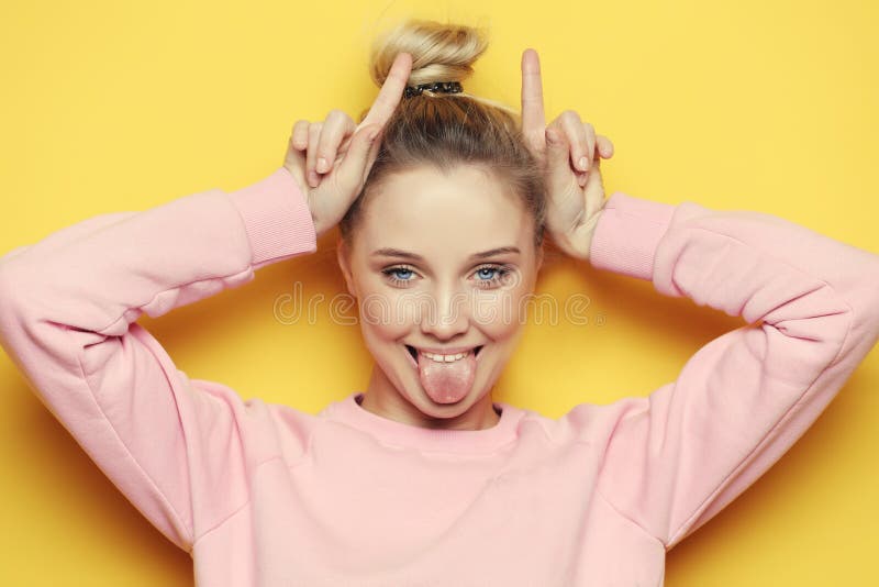 Portrait of playful young pretty blond woman showing horns and making faces. Isolated on yellow background. stock photos Portrait of playful young pretty blond woman showing horns and making faces. Isolated on yellow background. stock photos