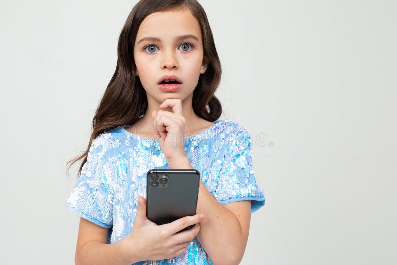 Closeup portrait of a teenager girl thoughtfully with open mouth holding a phone on an isolated white studio background