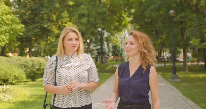 Closeup portrait of two female friends walking having conversation smiling cheerfully in park outdoors