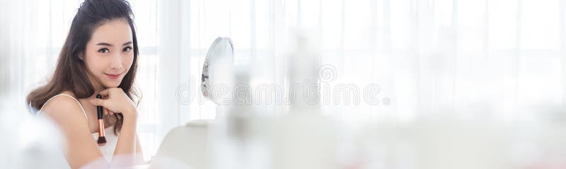 Closeup portrait of young beautiful asian girl using brush with mirror for makeup routine.