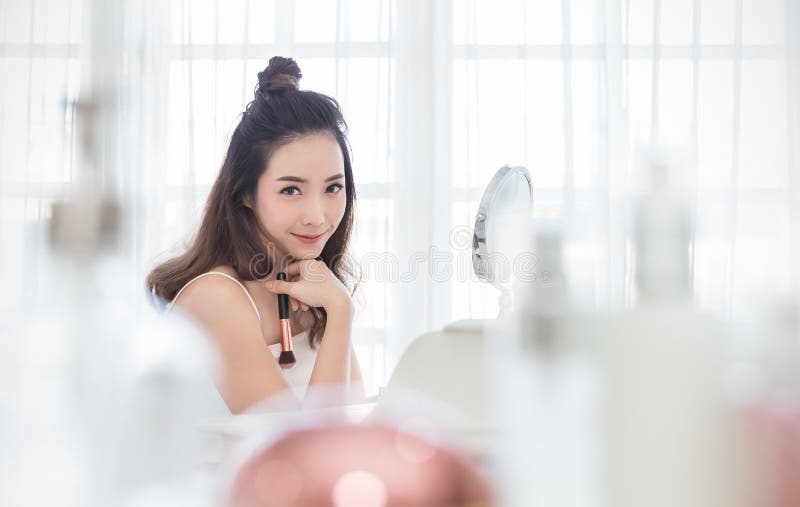 Closeup portrait of young beautiful asian girl using brush with mirror for makeup routine.