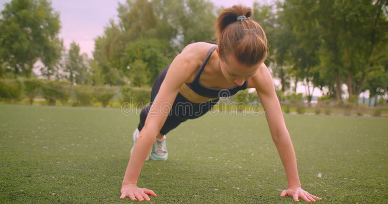 Closeup portrait of young beautiful sporty fitness girl standing in plank in the park in urban city outdoors