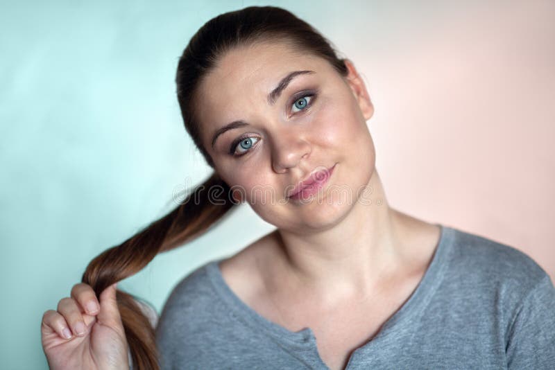 Closeup portrait of young brunette woman with blue eyes, smiling and curling her pony tail on vibrant cyan and pink background. royalty free stock photo